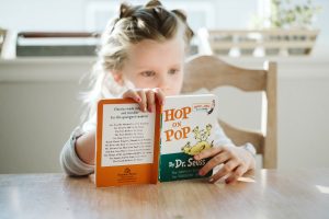 Little girl reading a Dr. Suess book at the kitchen table in her home over summer vacation. 